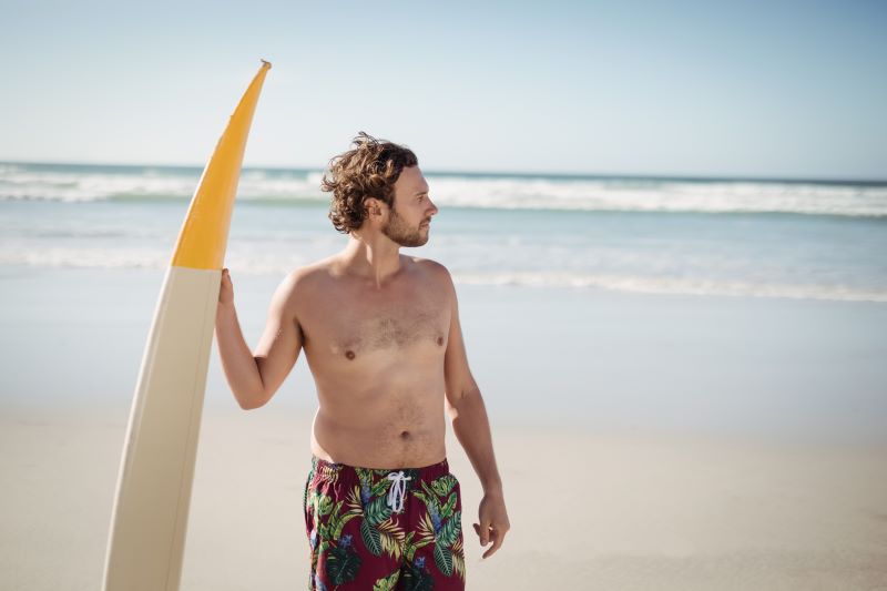 mężczyzna z deską surfingową na plaży po redukcji 